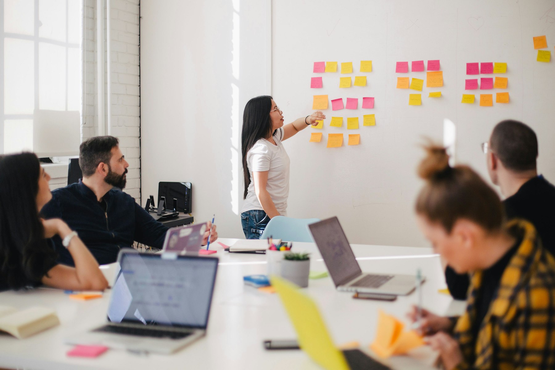 A person arranging coloured sticky notes on a wall while colleagues watch from a table