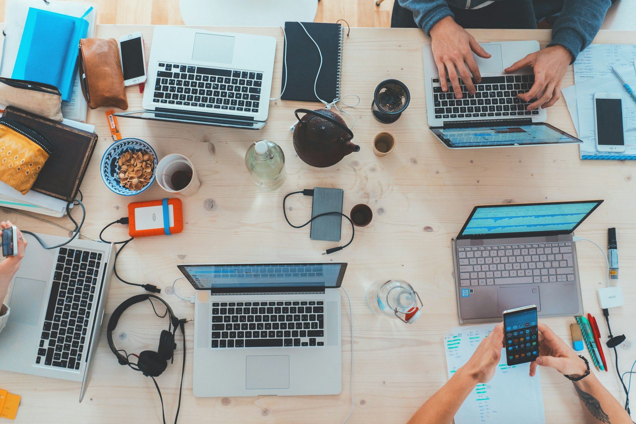 Overhead view of a shared work table covered with laptops, notebooks and devices